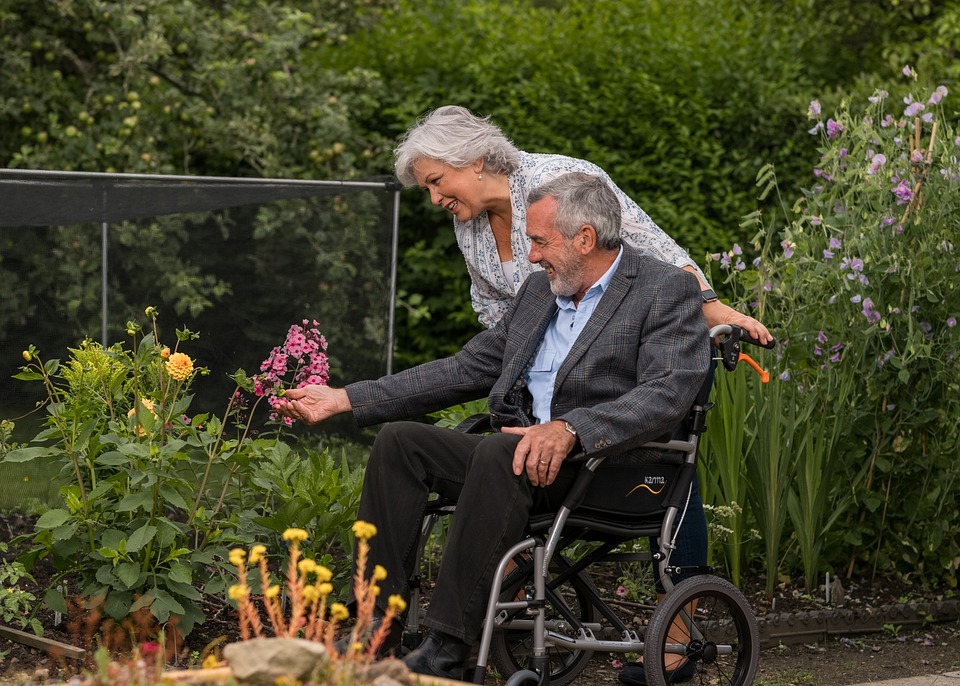 Man in a wheelchair with woman looking at flowers in a garden